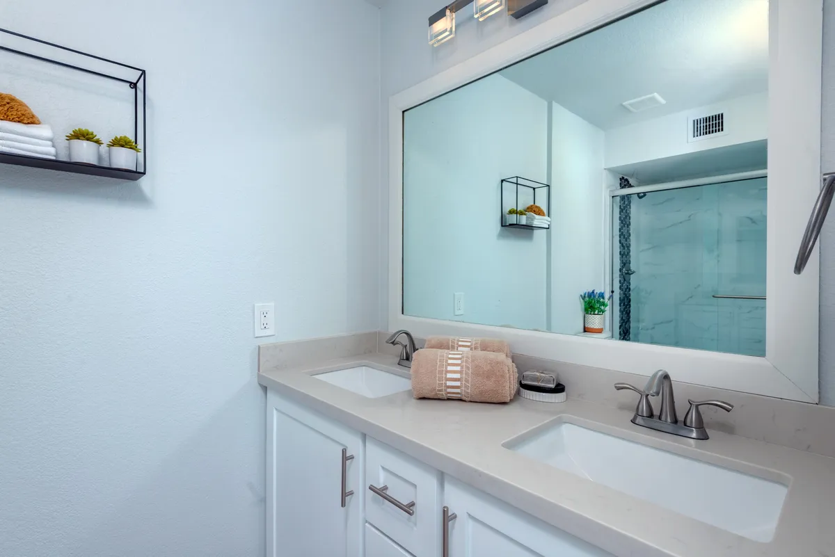 A bright, organized bathroom with double sinks, a large mirror, plush towels, and decorative shelving, providing a spa-like environment for self-care routines and relaxation.