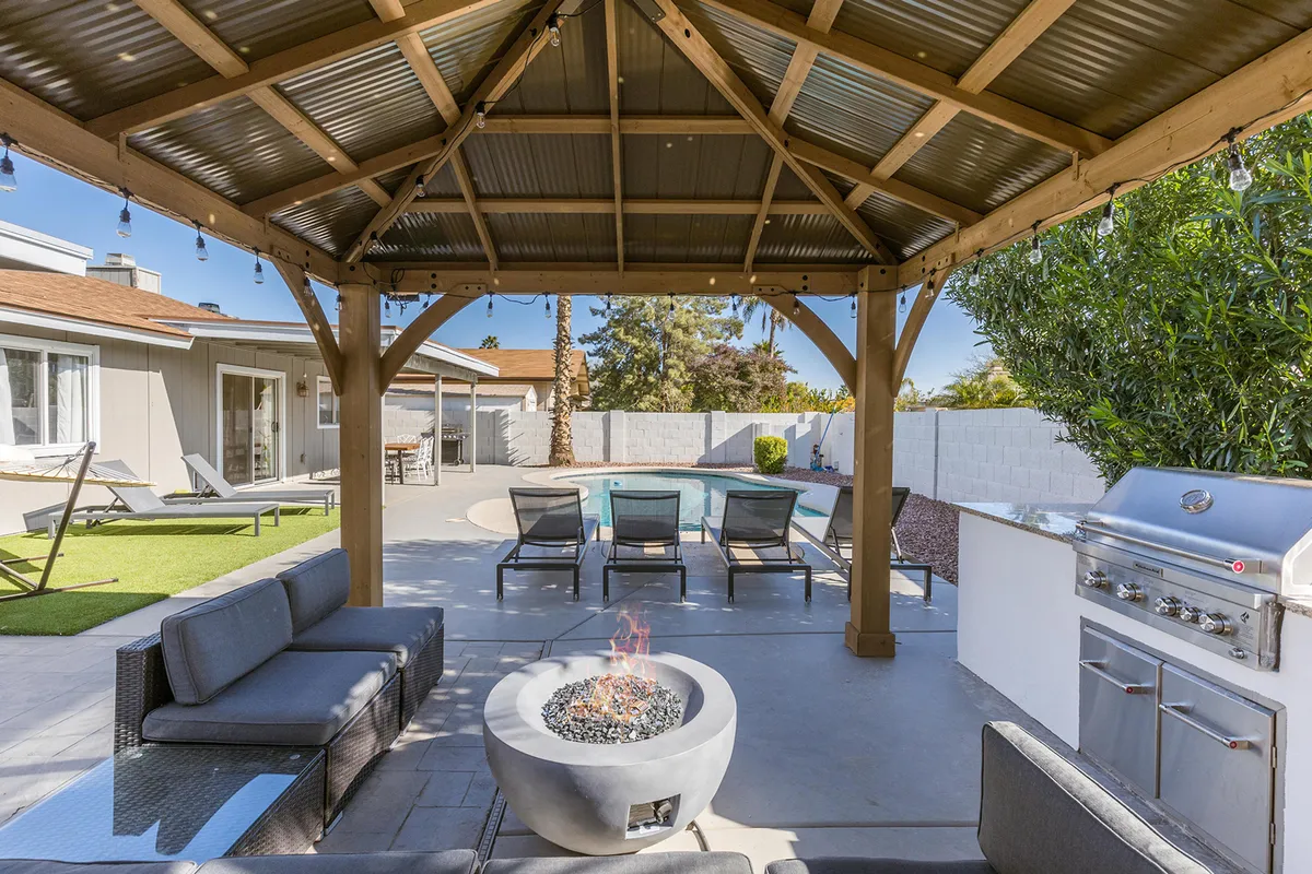 The photo features an outdoor seating area beside a fire pit, with the sparkling pool and a grill station visible in the background. The setup is perfect for social gatherings, barbecues, or evening fires with friends and family. The ambiance shifts from daytime fun to cozy nighttime entertainment, aligning with the section’s emphasis on versatility and evening enjoyment.