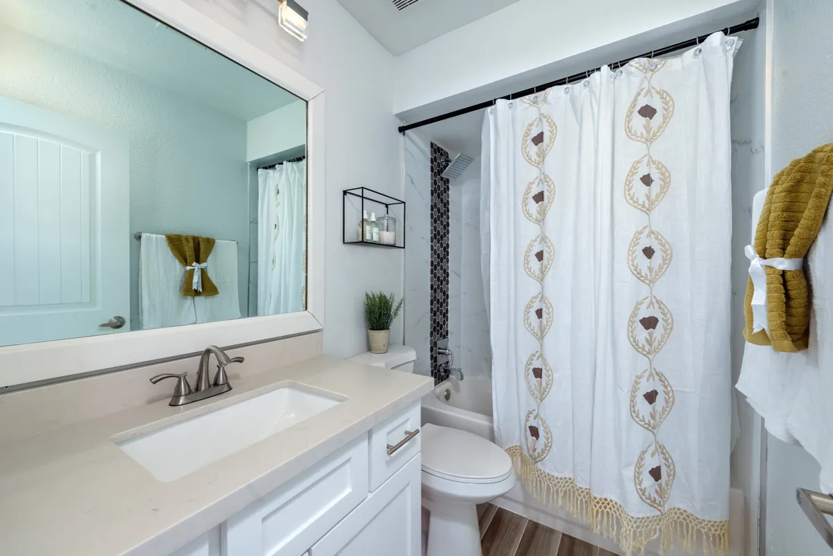 The image displays a fresh, inviting bathroom with a vanity, sink, decorative shower curtain, mirror, and bathroom accessories. The space feels clean and well-maintained, offering a sense of everyday luxury and attention to detail.