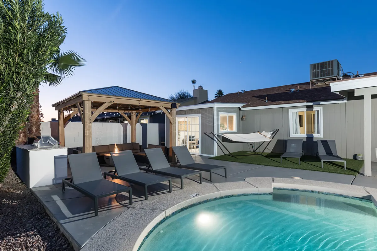 This image showcases a beautiful backyard with a pool surrounded by lounge chairs, a gazebo, and a hammock. The pool area is inviting, offering both sun-drenched spots for relaxation and shaded areas under the gazebo. The scene captures a tranquil, welcoming atmosphere with amenities ideal for socializing, swimming, and unwinding.