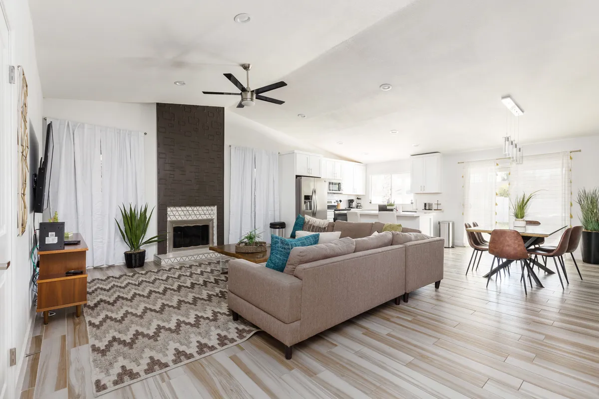 A spacious open-concept area encompassing a cozy living room with a sofa and fireplace, a dining table perfect for group meals, and a modern kitchen island in the background. The area is bathed in natural light, and the furniture is arranged for easy flow and conversation.