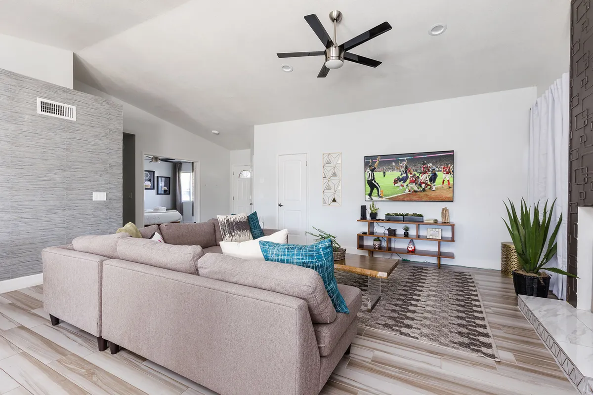 A comfortable sectional sofa faces a large TV displaying a sports scene, with decorative wall art and a potted plant adding style. The layout encourages relaxation and group socializing—ideal for unwinding after Scottsdale adventures.