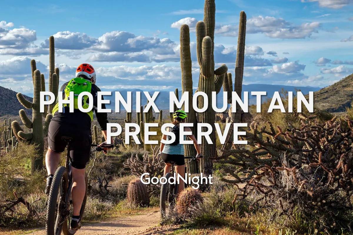 Two cyclists ride along a scenic desert trail lined with cacti and framed by a dramatic mountain backdrop, emphasizing the rugged beauty and outdoor adventure available in the Scottsdale area.