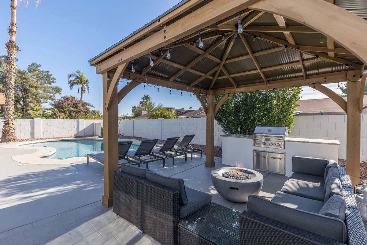 A beautiful backyard scene featuring a sparkling swimming pool, comfortable lounge seating, a grill station, a fire pit, and palm trees, ideal for social gatherings and relaxation after outdoor activities.