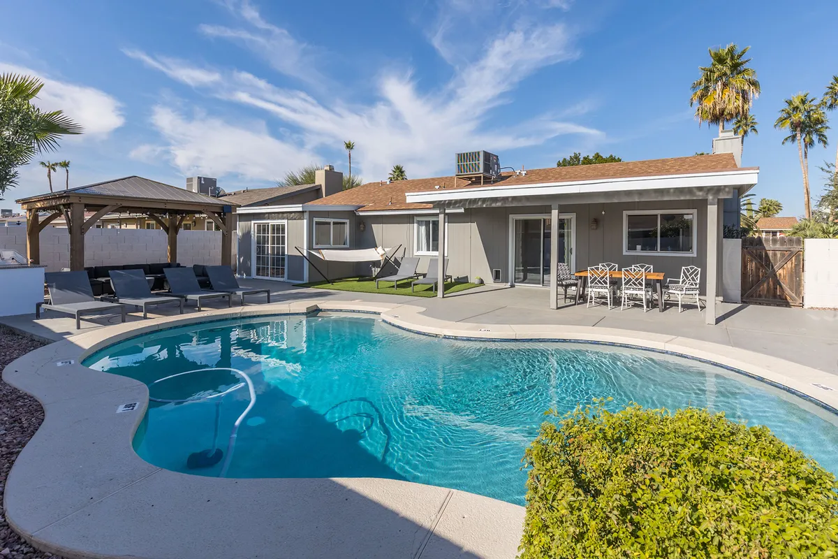 A sun-drenched outdoor space with a sparkling swimming pool, comfortable patio furniture, a hammock swaying gently between palm trees, and a shaded outdoor dining area. The setting is lush and vibrant, perfect for lounging and al fresco meals.